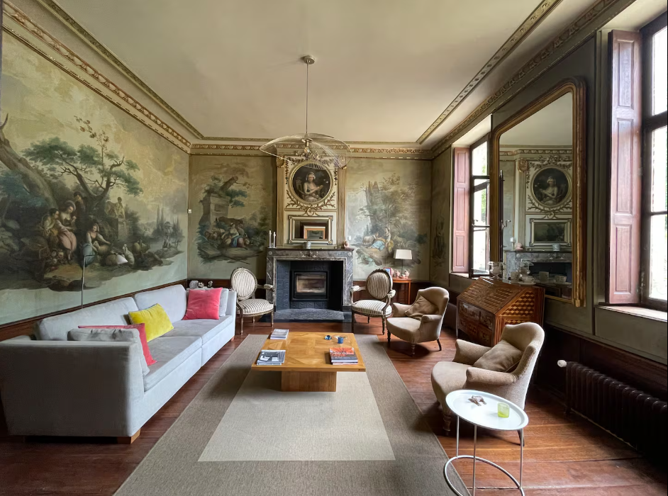 Salon of the mansion with painted pastoral murals, gilded cornices, a marble fireplace and low seating