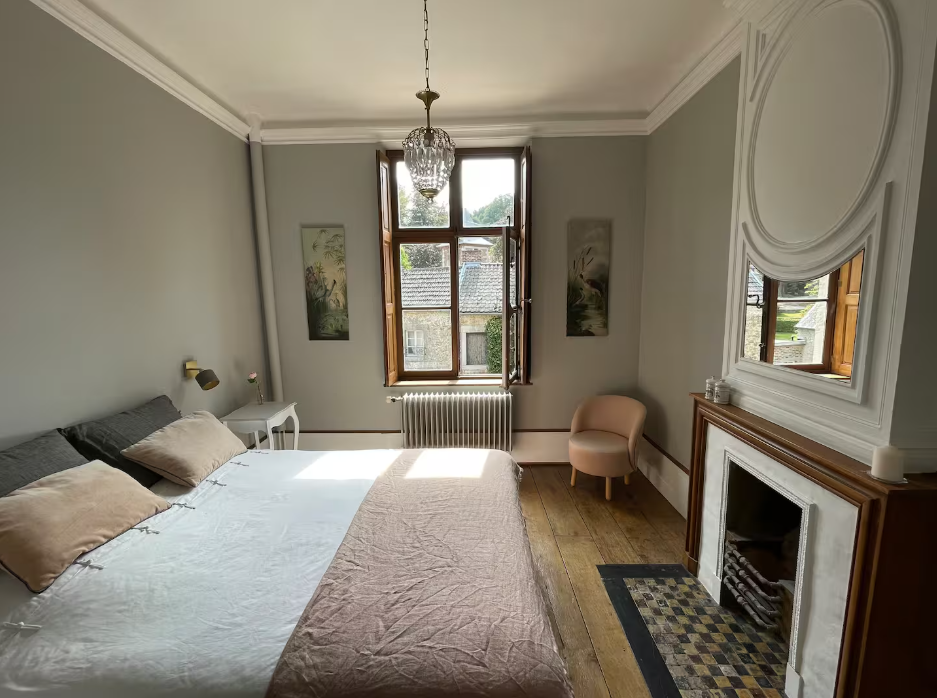 Bedroom with a large bed, tall shuttered window and a marble fireplace with mirror